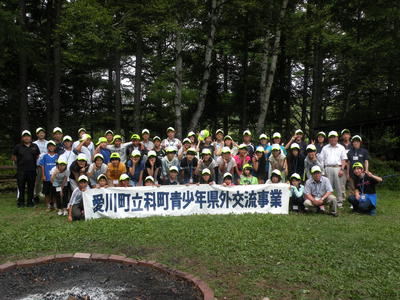 愛川町立科町青少年県外交流事業と書かれた横断幕を前列の参加者達が持ち、集合写真を撮っている写真