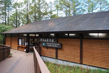 木製の歩道の奥に「御泉水自然園 ビジターセンター」と書かれた看板が建物に掛かっている御泉水自然園 ビジターセンターの外観写真