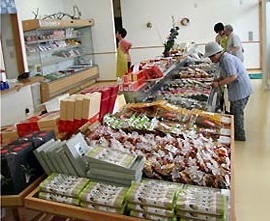 沢山の商品が棚に並べられ、買い物客が商品を見ている農産物直売所内の写真