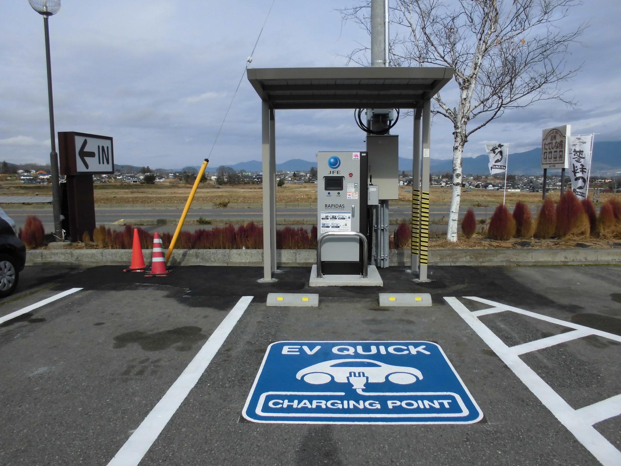 駐車スペースの地面に「EV QUICK CHARGING POINT」の文字と車のイラストが描かれ、奥に電動車両用急速充電器が設置されている写真