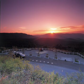 奥に見える山の山頂に沈んでいく夕日の写真