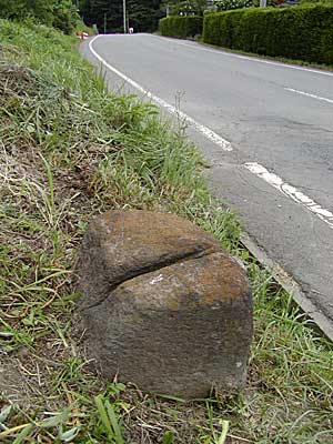 上り坂の道路の道端に置かれた丸みを帯びた大きな石の中央に切り込みが入っている切り石の写真