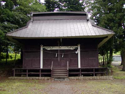 木々に囲まれた場所にあり、正面に紙垂の付いたしめ縄が掛けられている木造の諏訪神社の外観写真