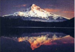 山頂に雪が積もっており、薄暗い中にオレンジ色の光が指している山が水面にも写っている山の写真
